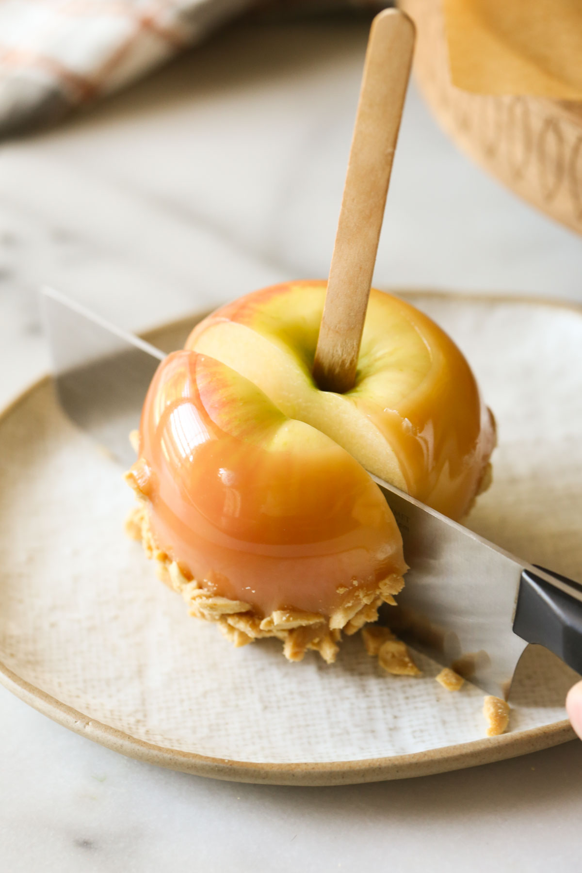 A Homemade Caramel Apple on a plate being sliced with a knife.  