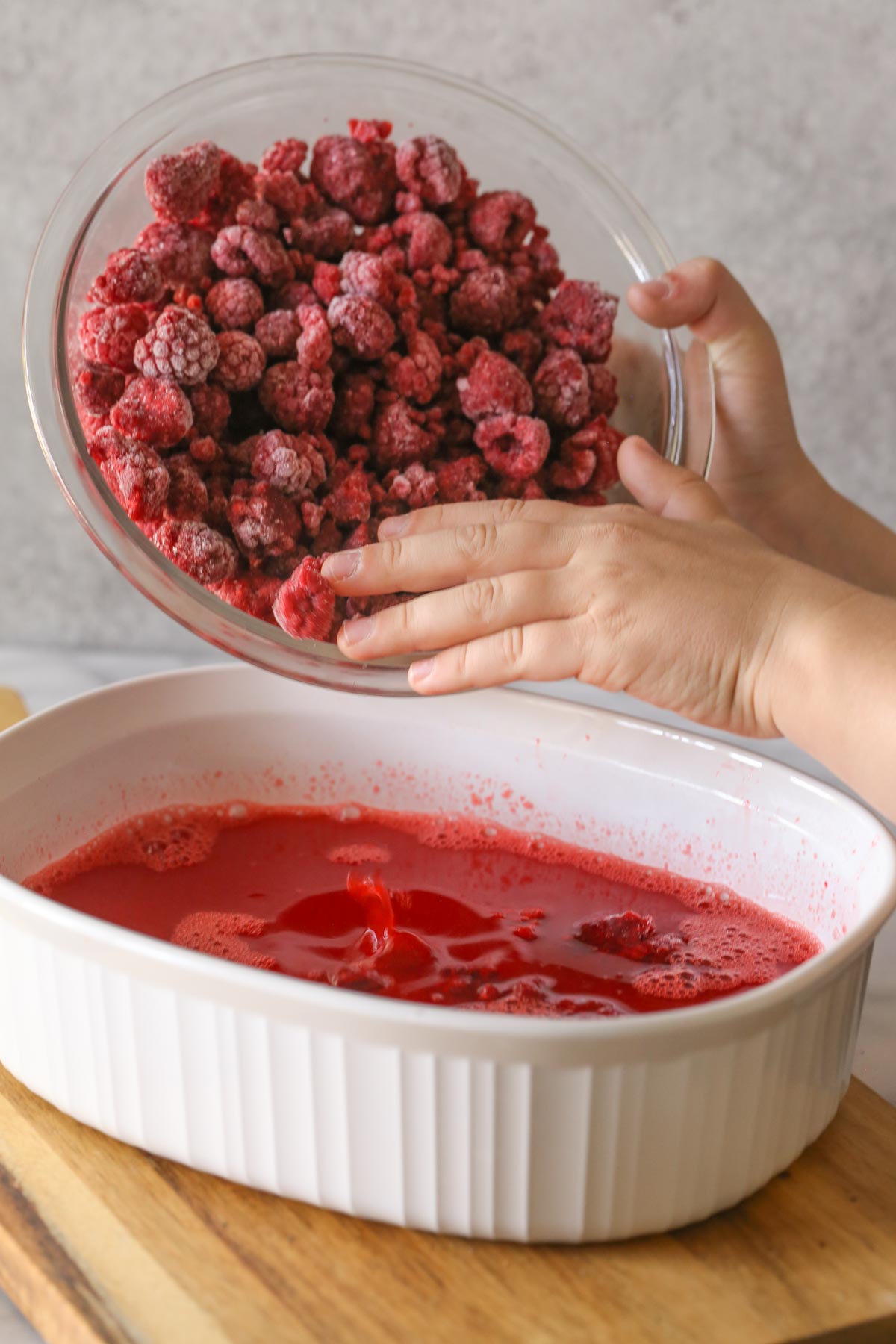 A bowl of frozen raspberries being poured into a baking dish with the other ingredients for the Raspberry Jello Salad. 