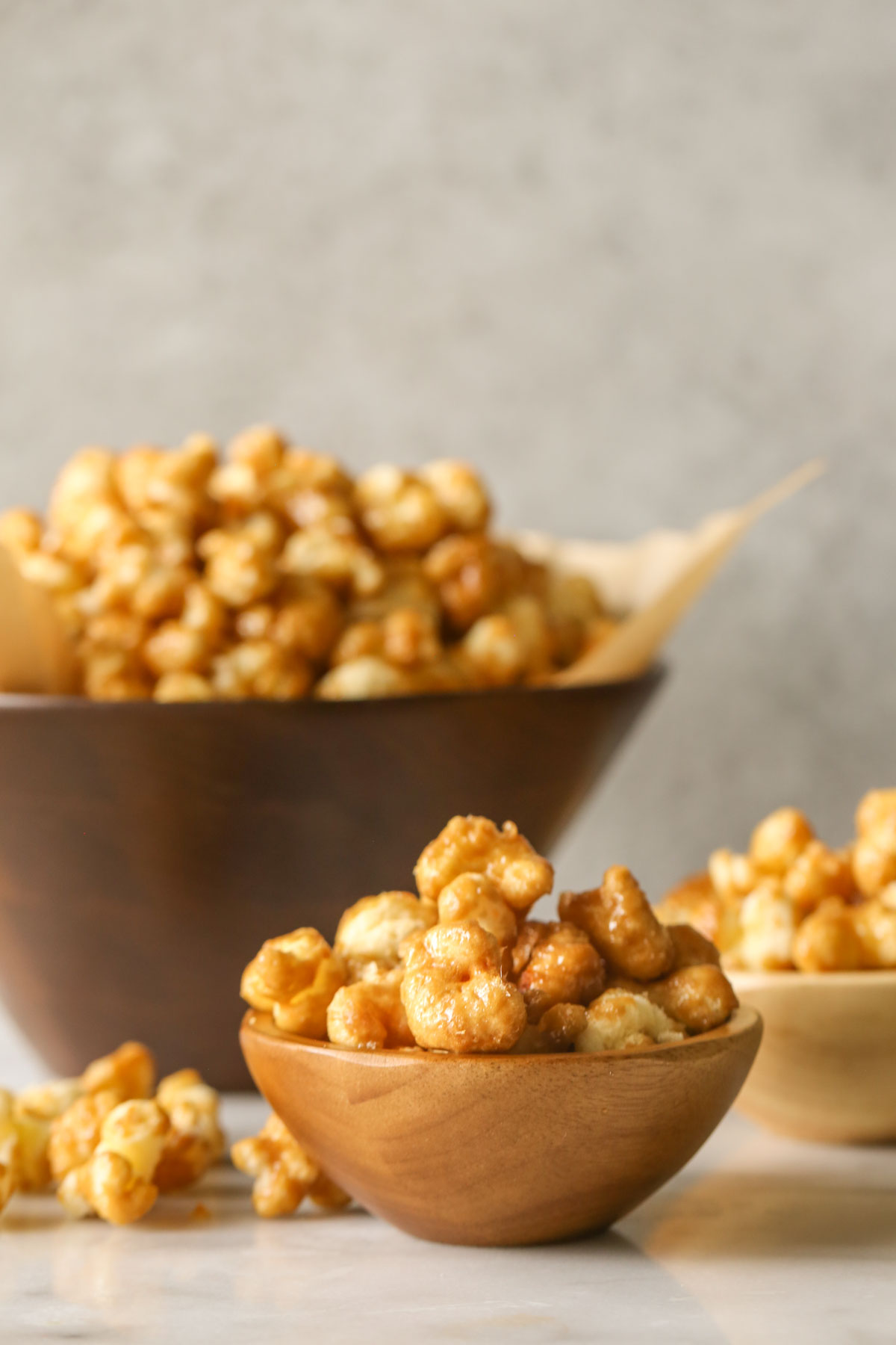 A small wood bowl of Caramel Puff Corn, with another small bowl and a large wood bowl of Caramel Puff Corn in the background.  