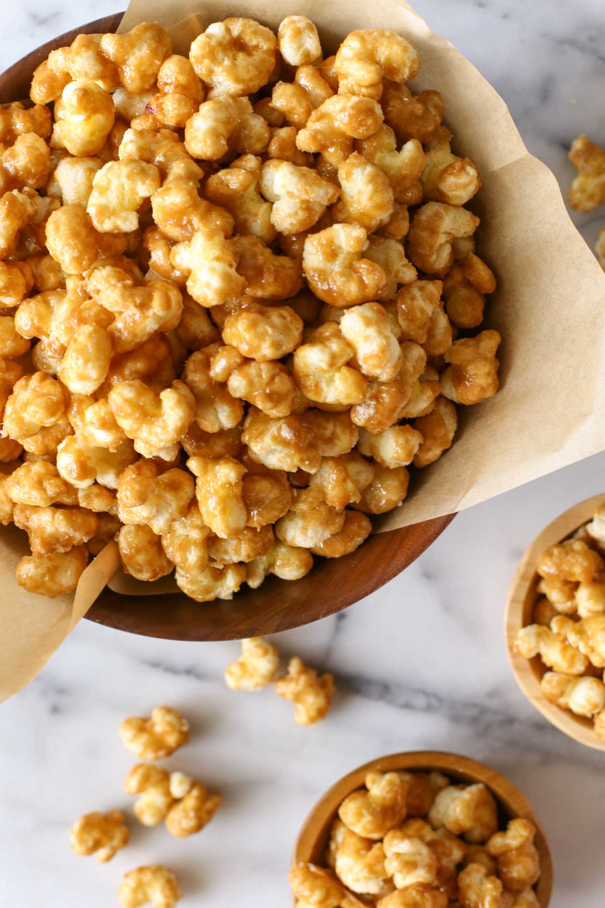 Overhead shot of Caramel Puff Corn in a wood bowl lined with parchment paper, with two small wood bowls of Caramel Puff Corn next to it.  