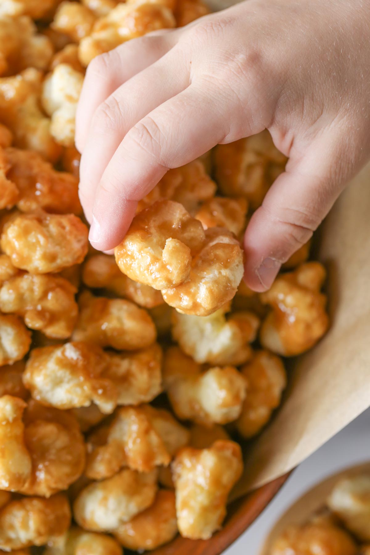 Close up shot of a hand grabbing Caramel Puff Corn from a wood bowl lined with parchment paper.  
