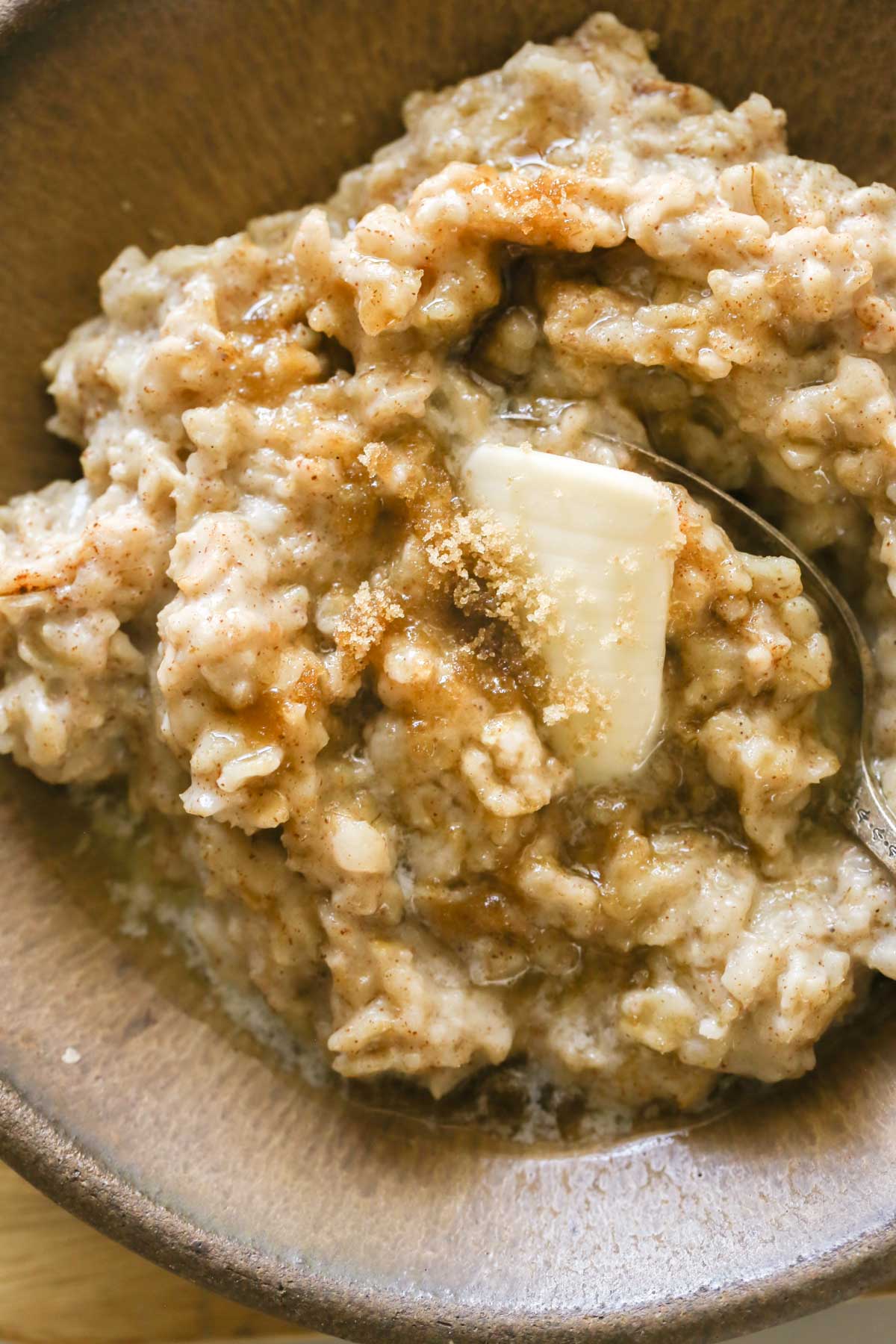 Close up shot of a bowl of oatmeal topped with butter and brown sugar.  