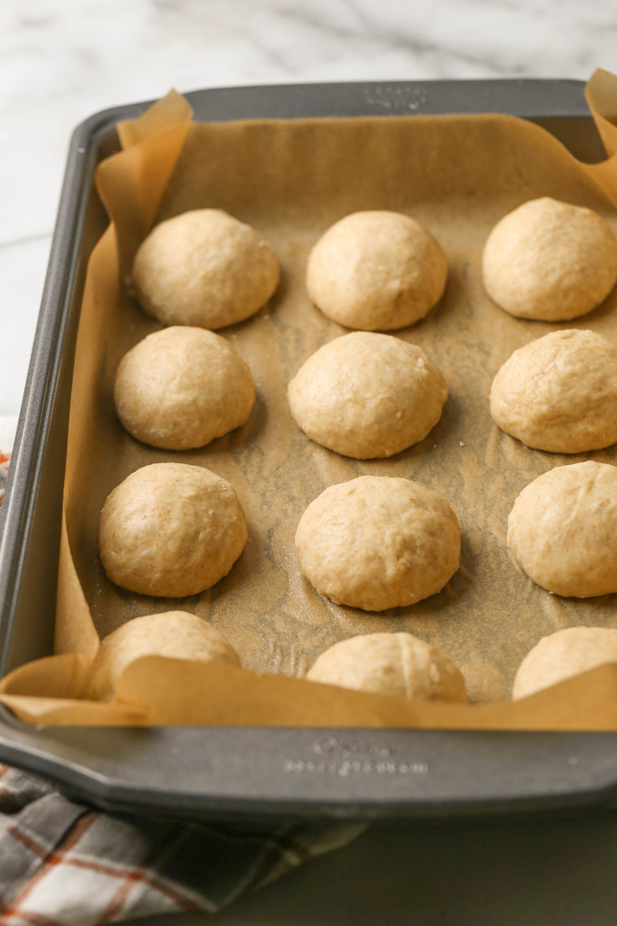 A baking pan lined with parchment paper with the dough balls for the Overnight Honey Wheat Rolls spaced out evenly.  