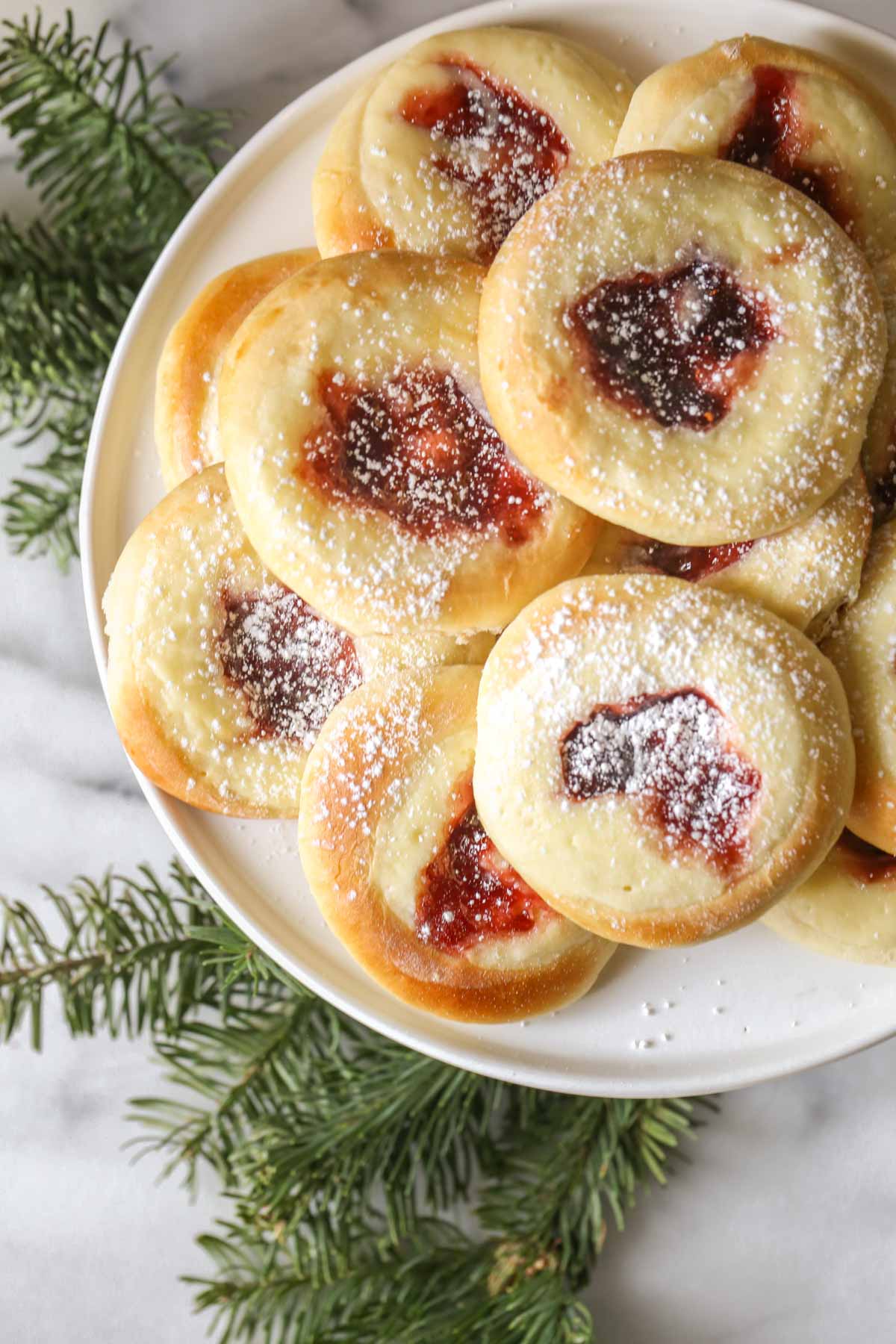 Overhead shot of Raspberry Cream Cheese Kolaches arranged on a cake stand, with a marble background and some pine tree branches. 