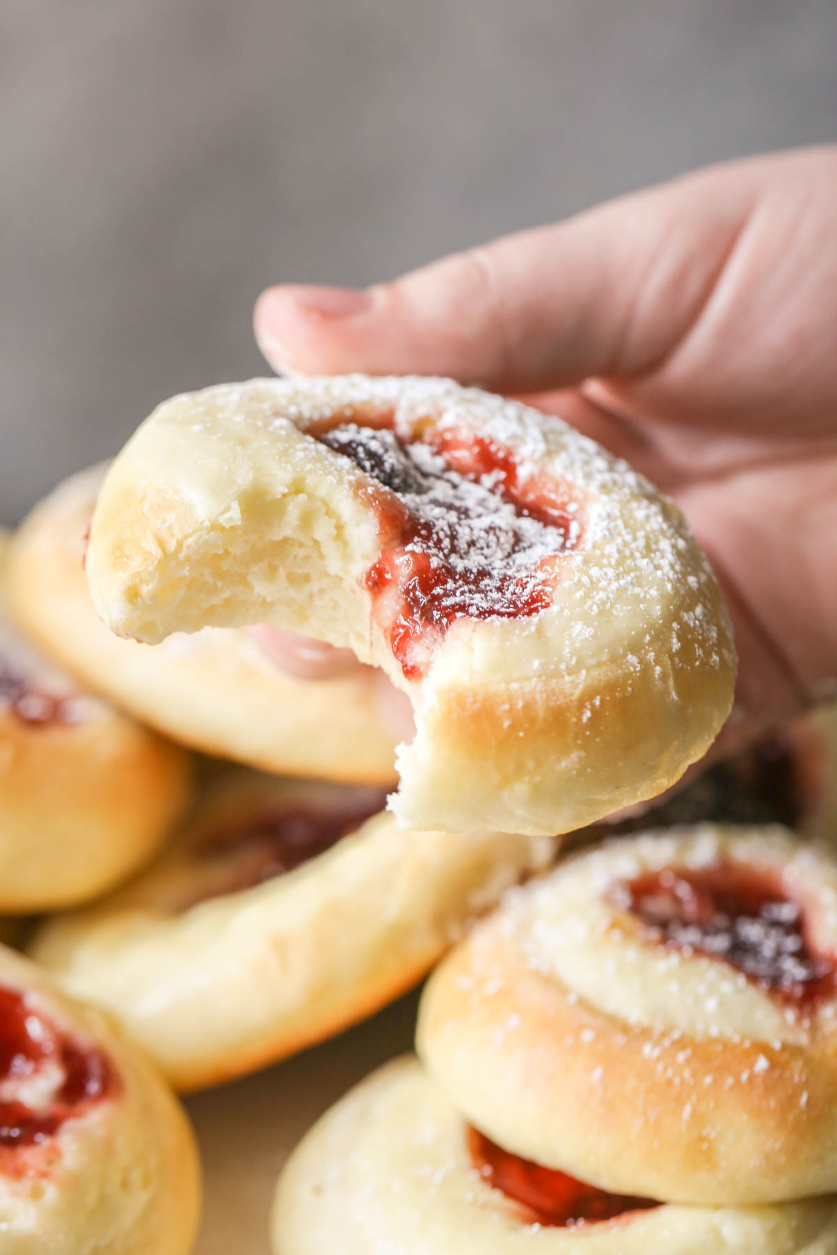 Close up shot of a hand holding a Raspberry Cream Cheese Kolache with a bite missing, with more Raspberry Cream Cheese Kolaches in the background. 