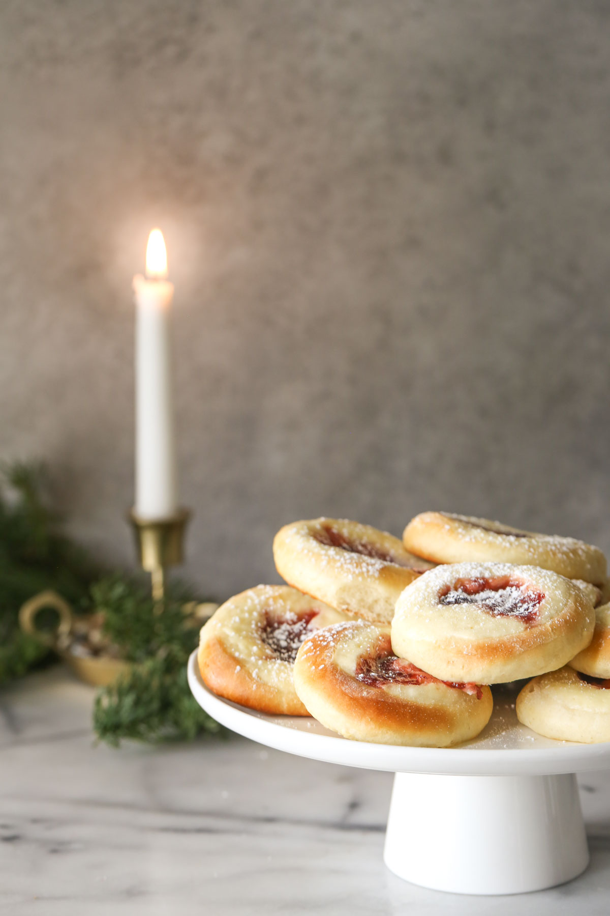 Raspberry Cream Cheese Kolaches arranged on a cake stand, with a candle burning in the background.  