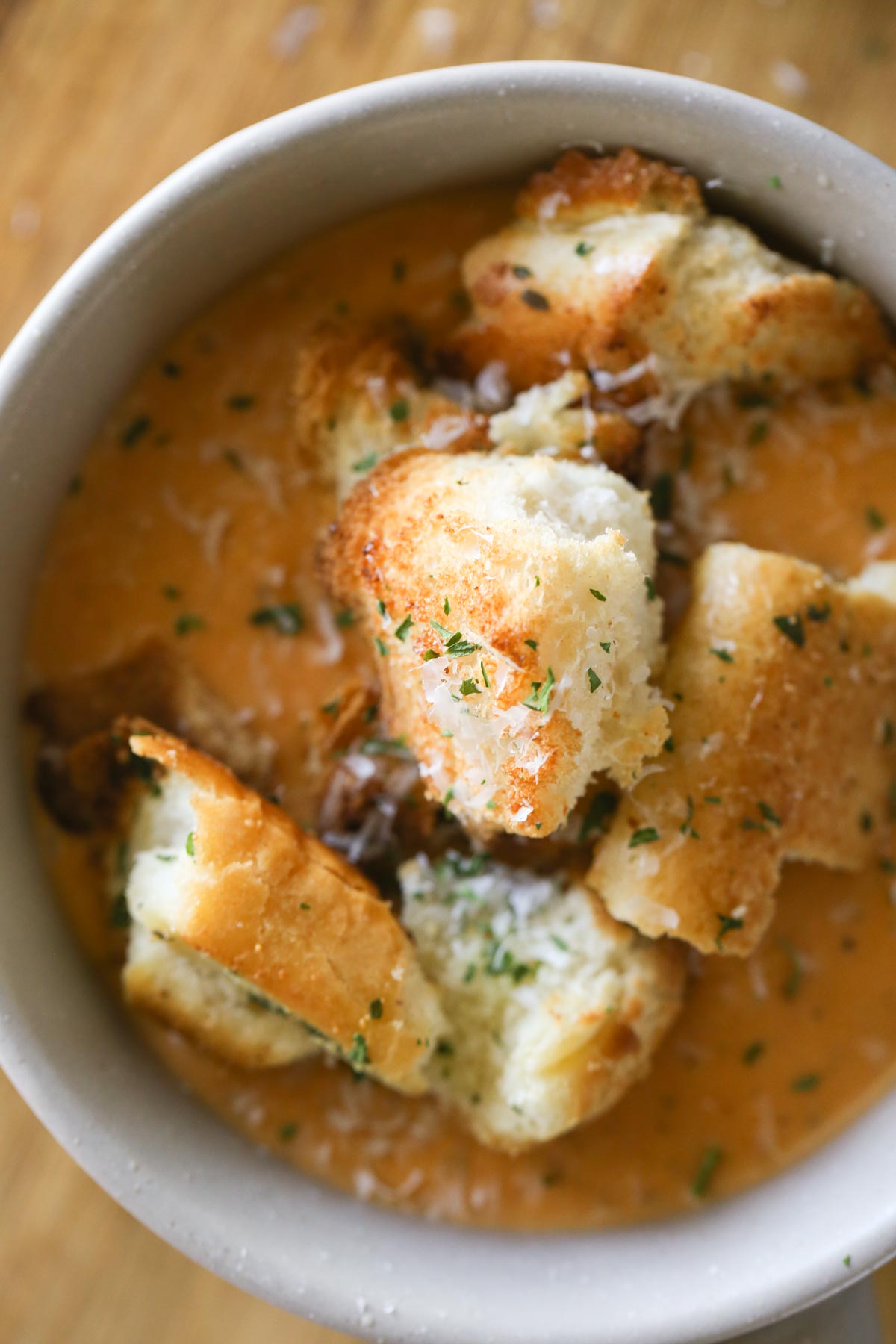 Overhead shot of a bowl of soup topped with Rustic Buttery Garlic Croutons and sprinkled with fresh Parmesan cheese. 
