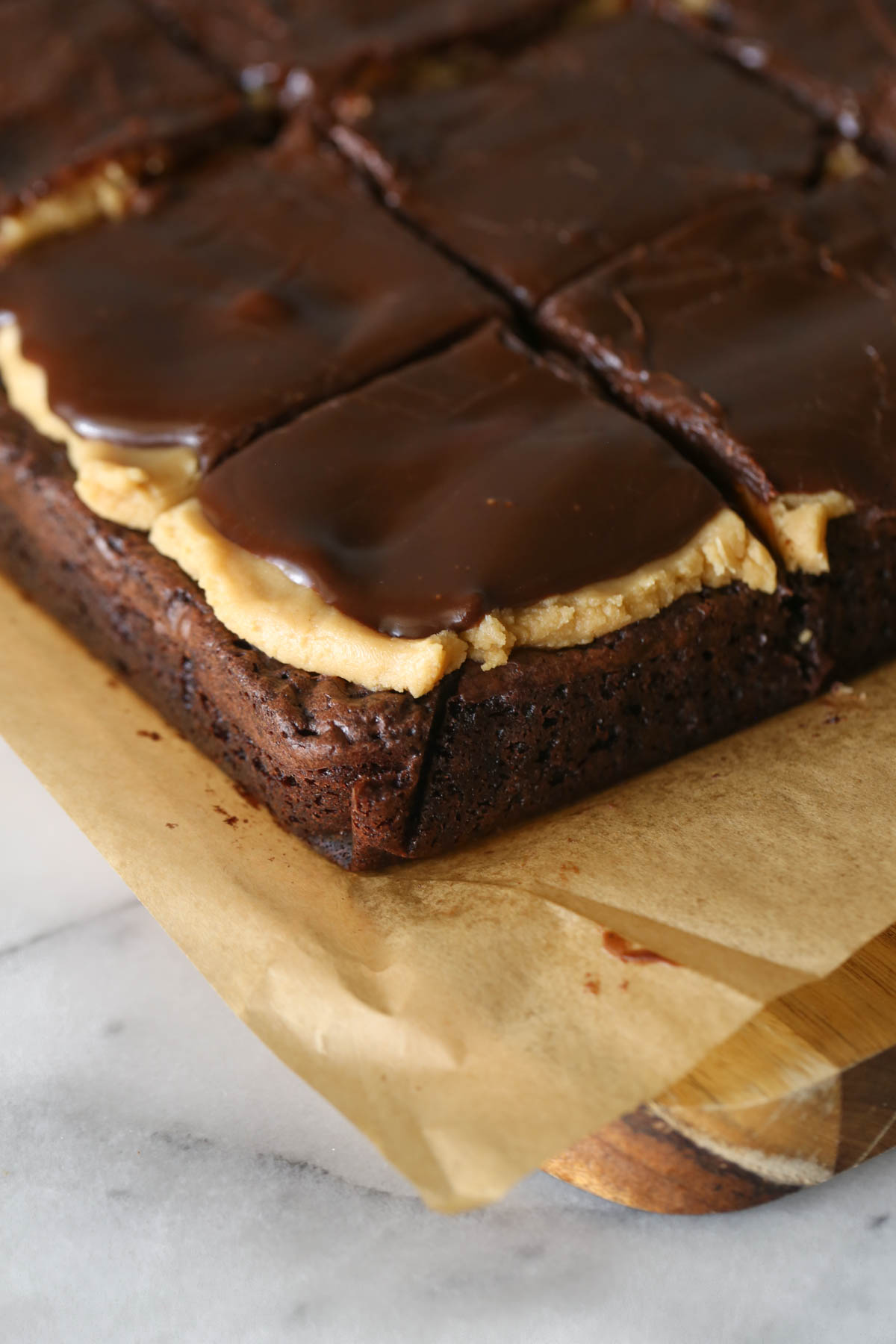 Close up shot of Chocolate Peanut Butter Brownies on parchment paper, sitting on a wood cutting board.  