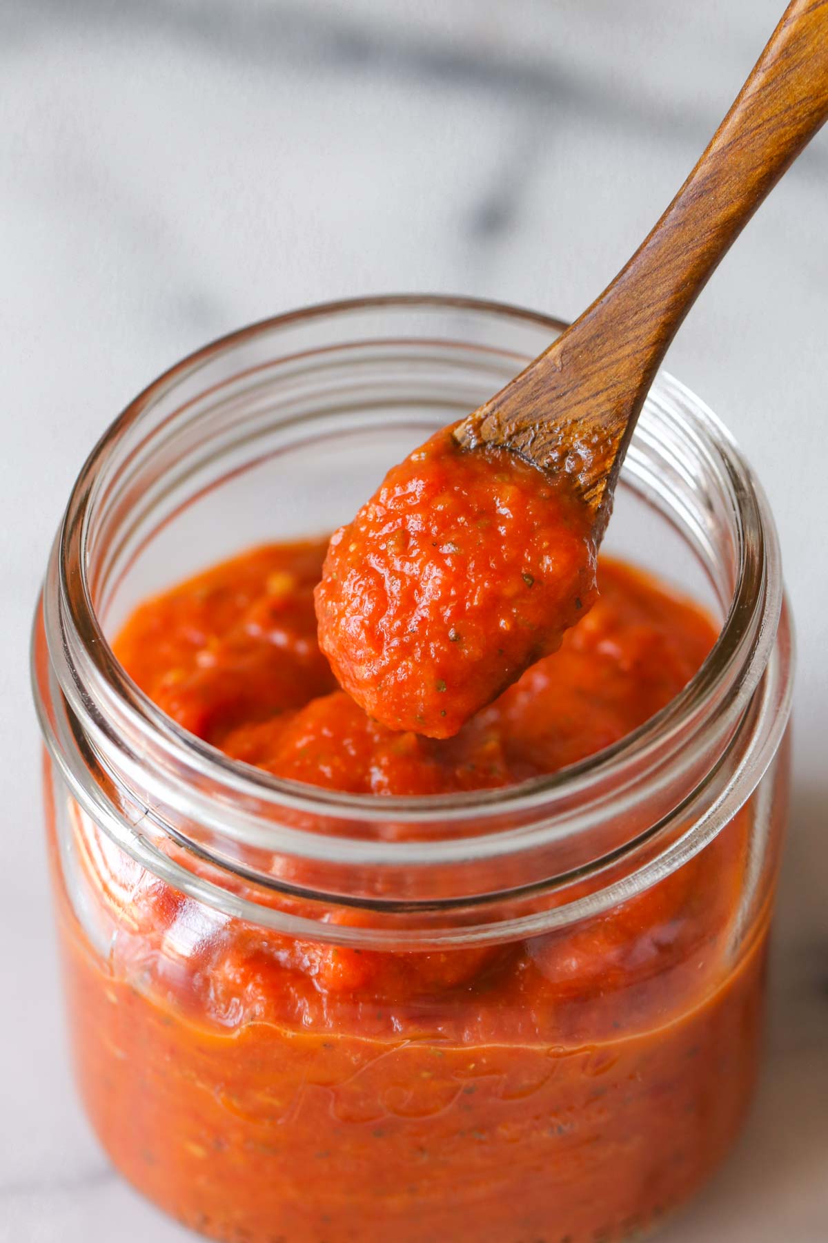 Close up shot of a small wooden spoon full of Roasted Tomato Pizza Sauce that has been scooped out of a jar of Roasted Tomato Pizza Sauce. 