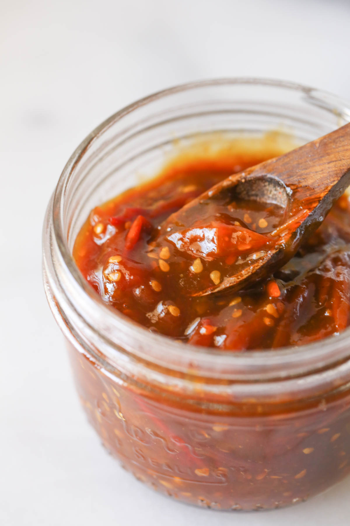 Close up shot of Tomato Jam in a small glass jar with a tiny wooden spoon in it.  