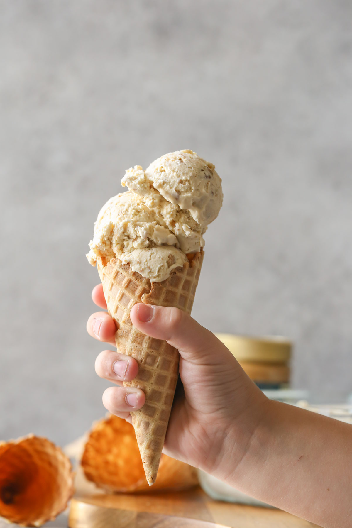 A hand holding a waffle cone with Cookie Butter Crisp Ice Cream.