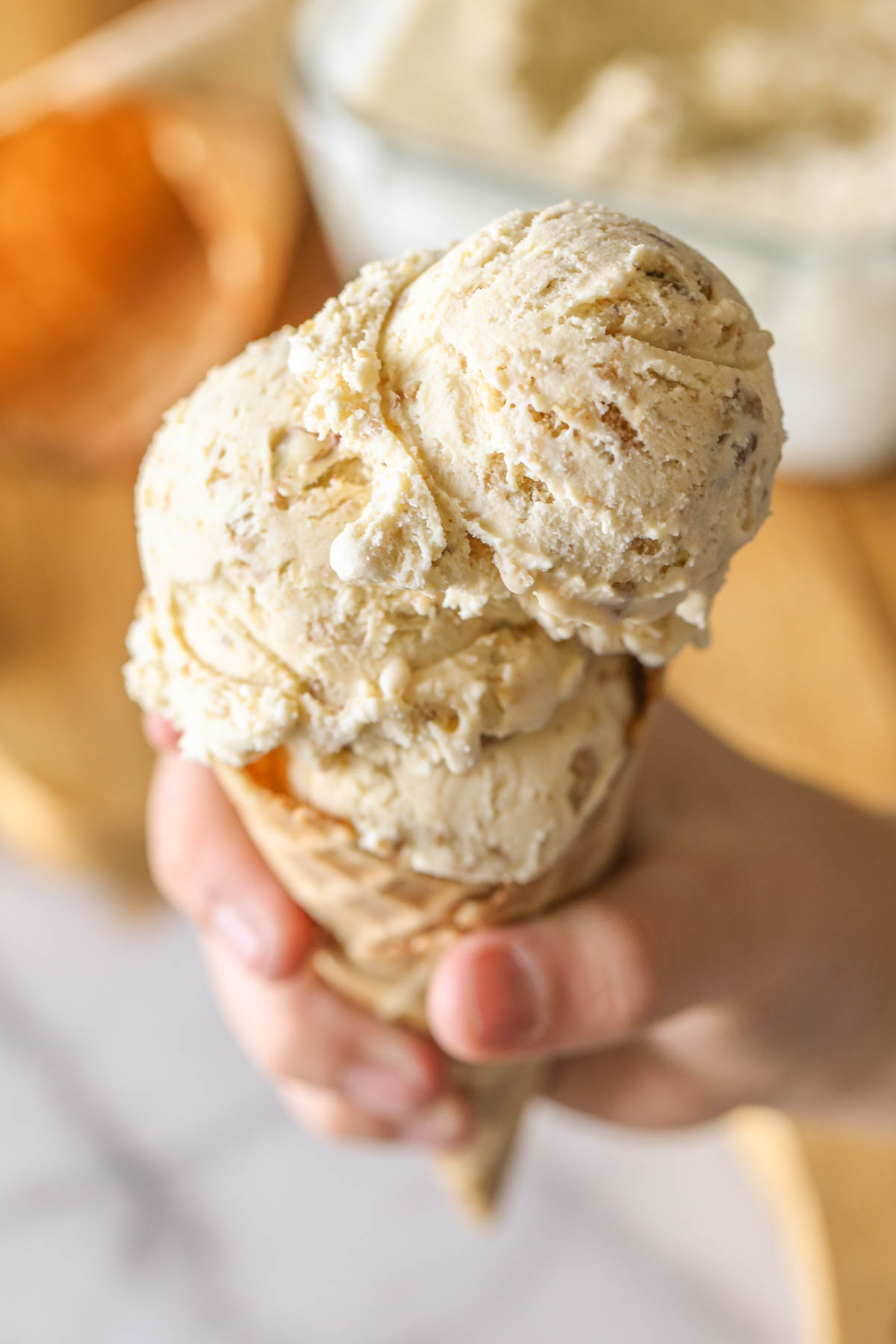 Close up shot of Cookie Butter Crisp Ice Cream in a waffle cone with a hand holding it. 