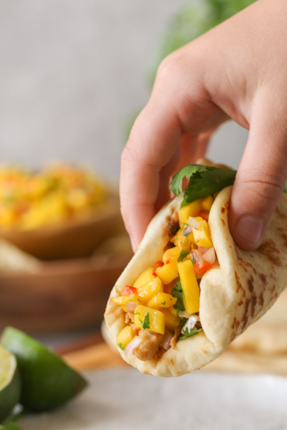 Close up shot of a hand holding toasted naan bread filled with Buttery Honey Chipotle Chicken and topped with Mango Lime Salsa.