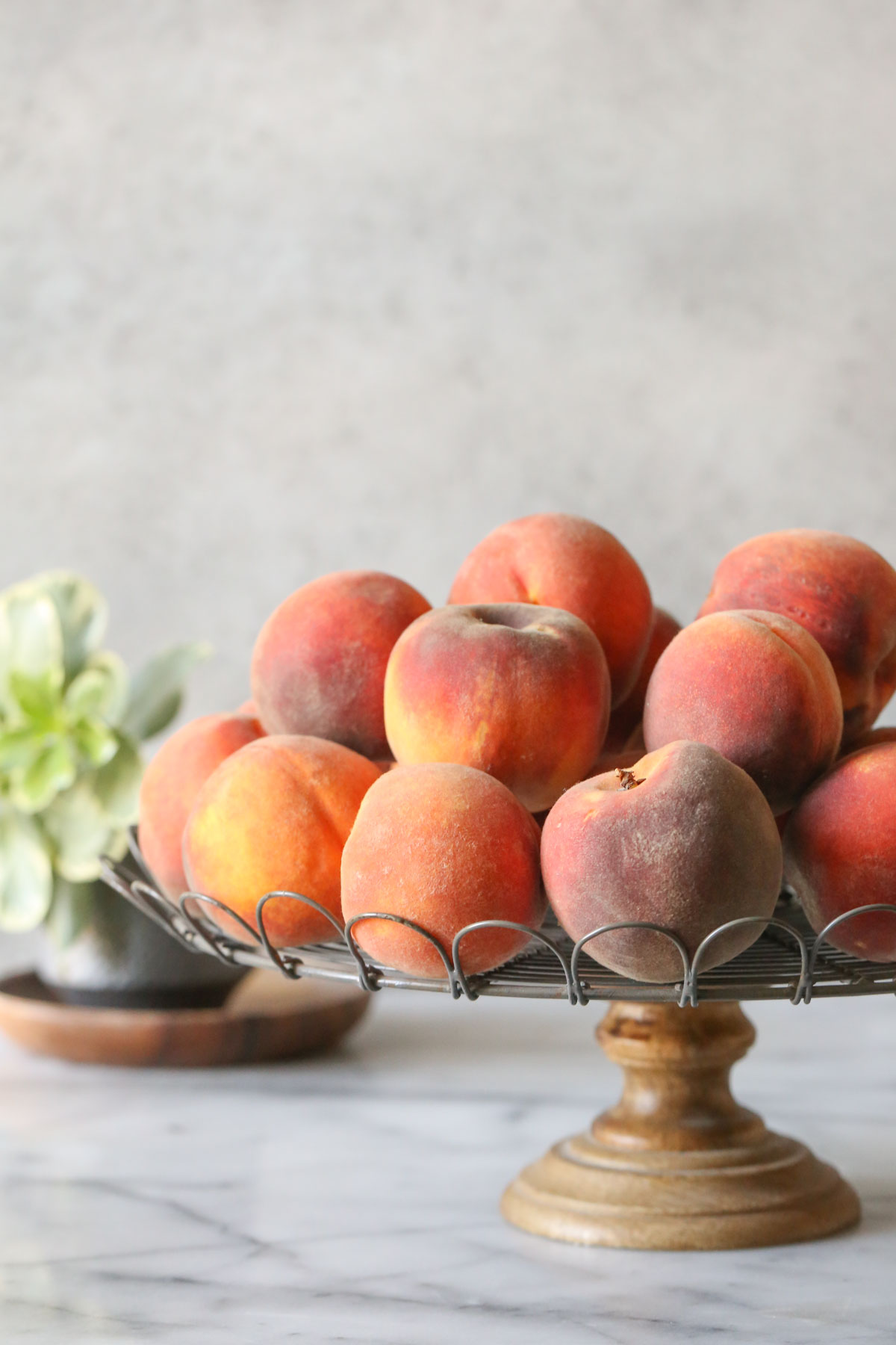 A cake stand with peaches piled on top of it.  