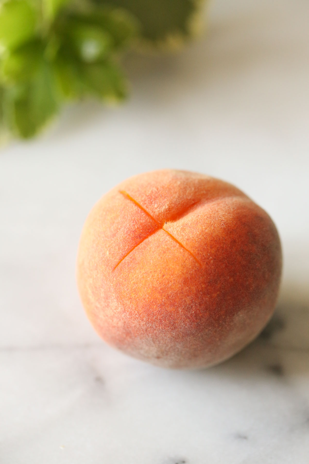 Close up shot of a peach with an "X" cut into the bottom of it.  