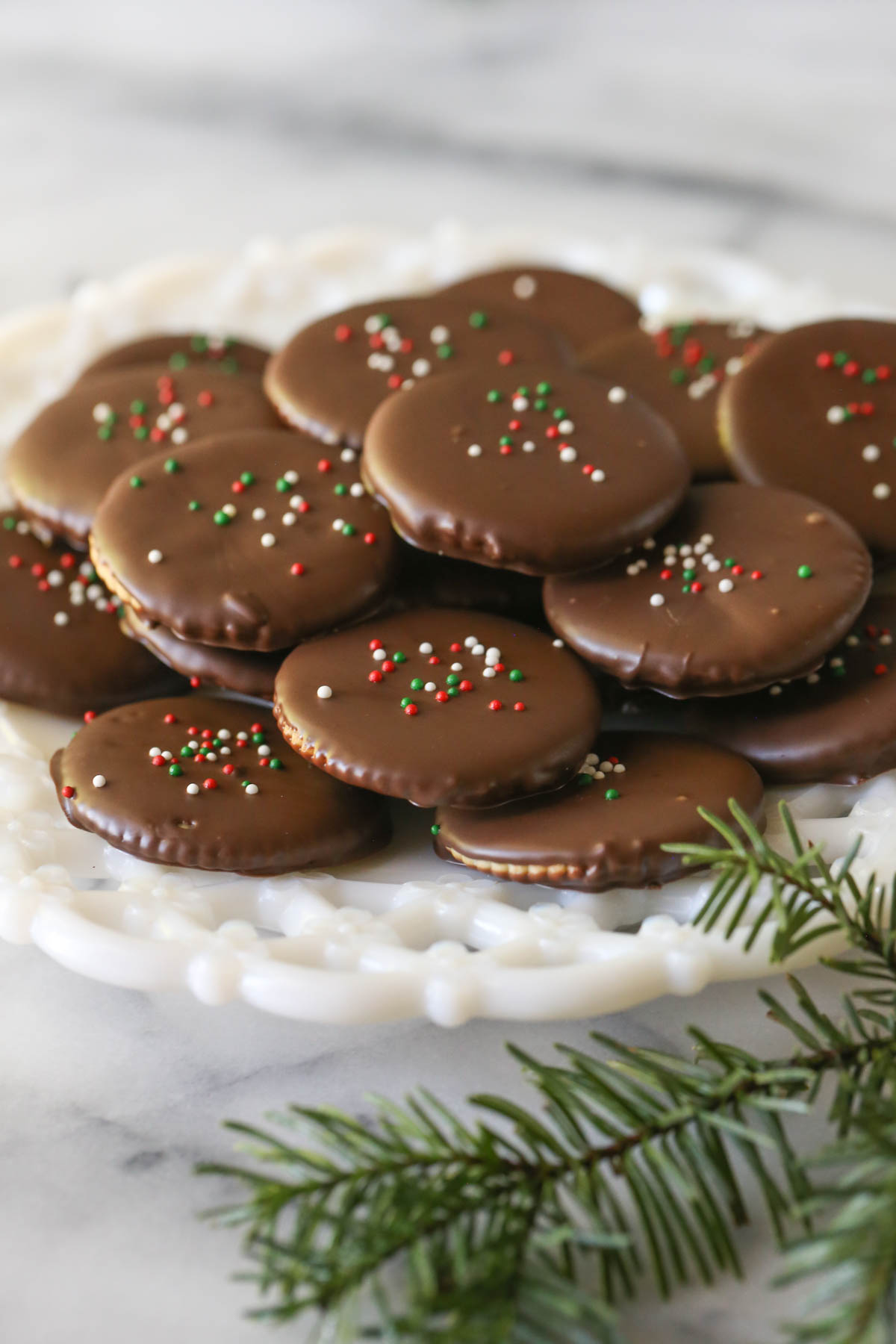 Copycat Thin Mints arranged on a white decorative plate on a marble background with some pine greenery. 