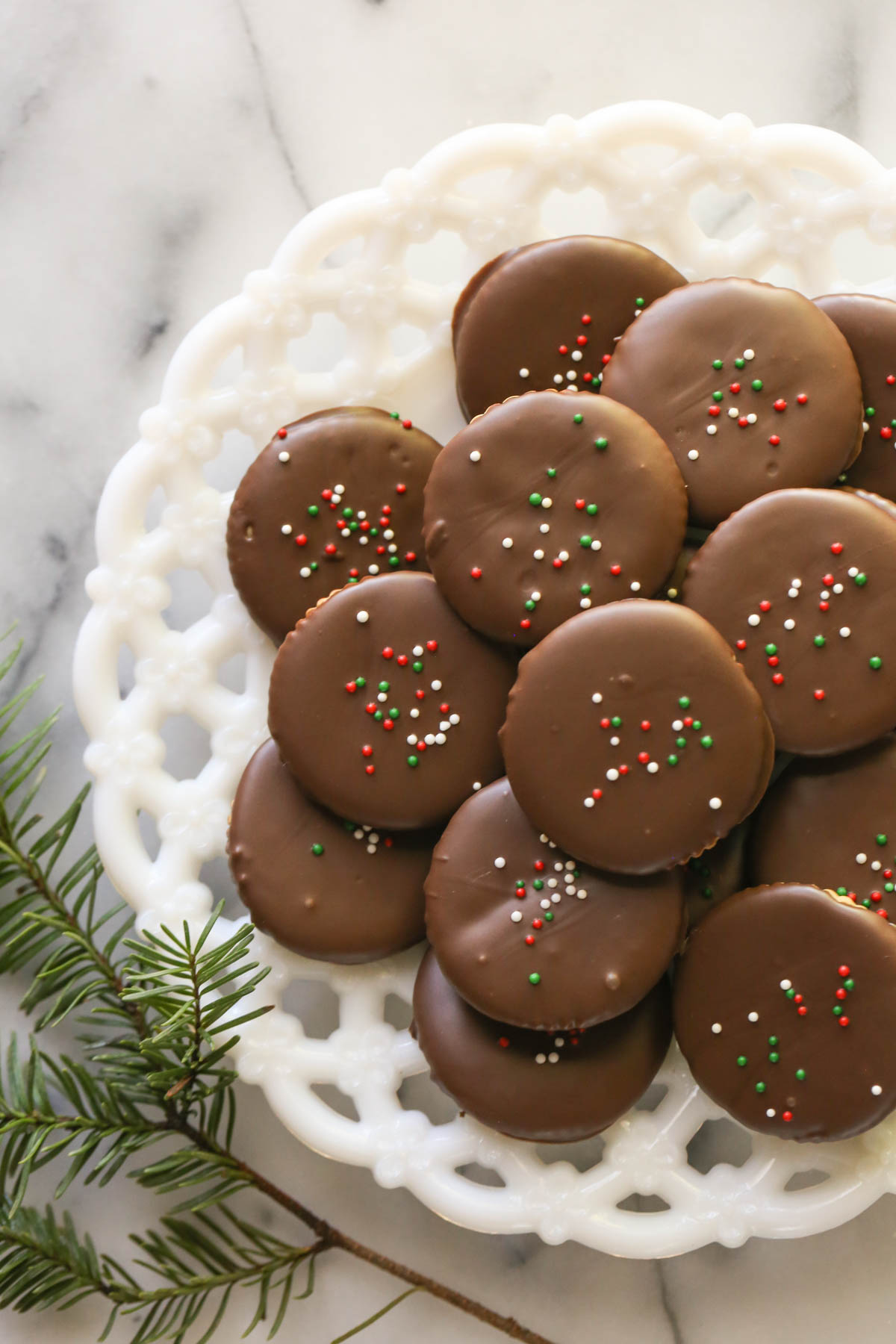 Overhead shot of Copycat Thin Mints arranged on a white decorative plate on a marble background with some pine greenery. 