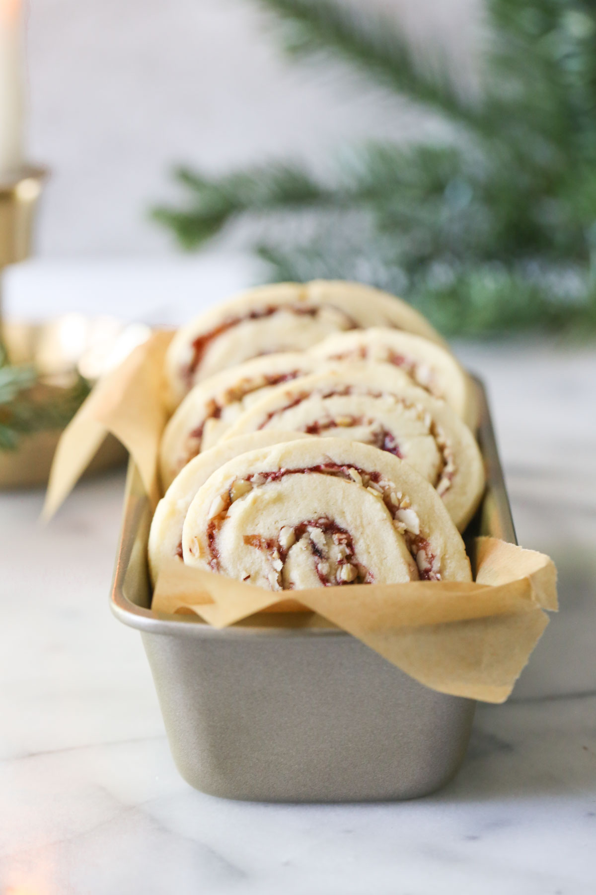 Raspberry Almond Pinwheels arranged in a parchment paper lined mini loaf pan, with a candle and greenery in the background.  