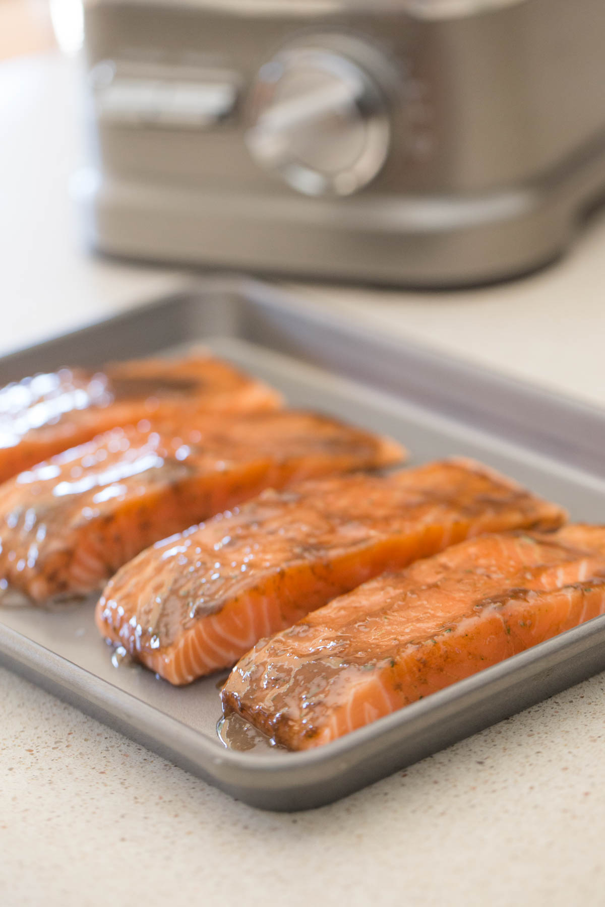 Four fillets of salmon on a baking sheet with the Honey Mustard Balsamic marinade spread on each fillet. 