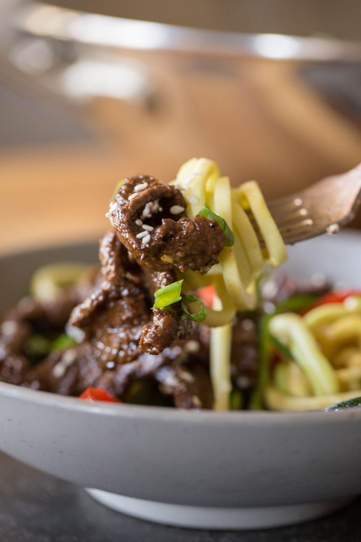Close up shot of a fork full of Spicy Korean Beef and Zoodles held over a bowl of Spicy Korean Beef and Zoodles. 