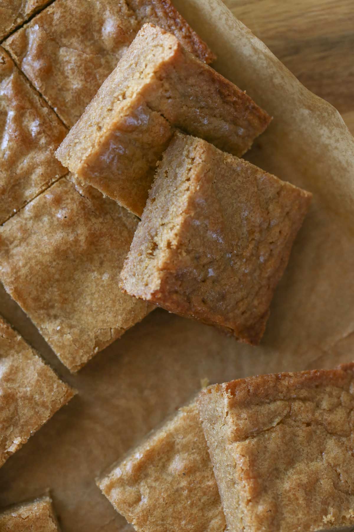 Close up overhead shot of Best Ever Blondies cut into square bars on parchment paper on top of a wood cutting board.