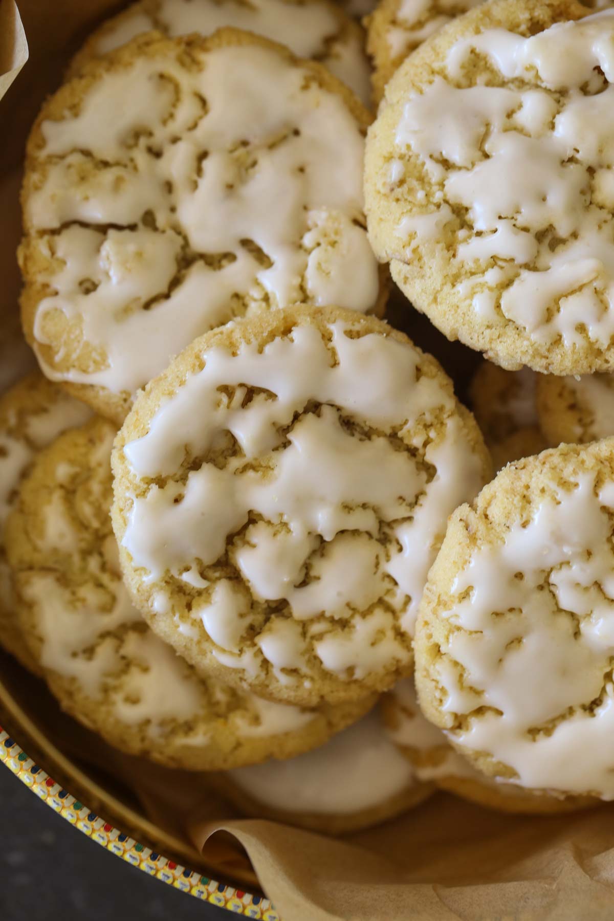 Close up overhead shot of Iced Lemon Oatmeal Cookies stacked in a parchment paper lined cookie tin.  